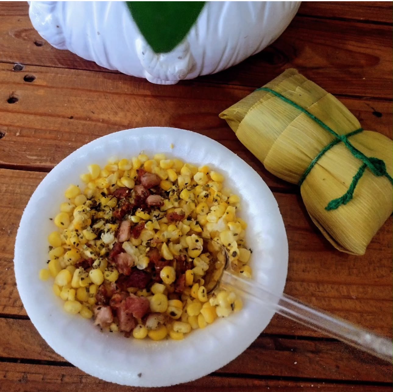 Prato de milho com bacon e temperos ao lado de uma pamonha artesanal